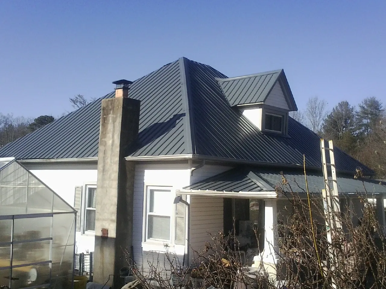 Dark blue standing seam metal roof on a white farmhouse with dormer — Slate & Tile Roof Repair by Roofing Brothers in Del Valle