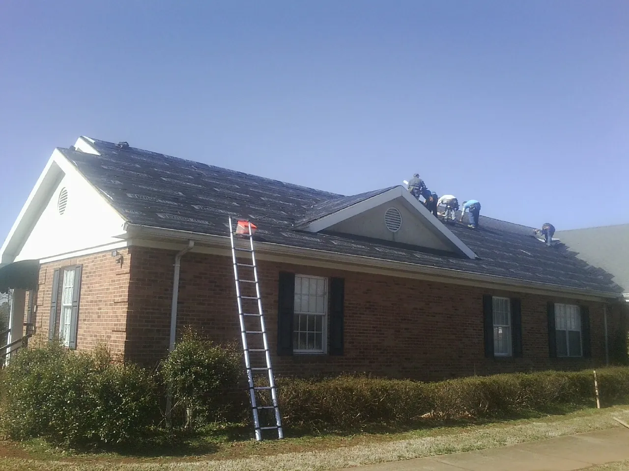 Crew tearing shingles off a brick ranch roof with a ladder set — Emergency Roof Repair work by our crew in Del Valle