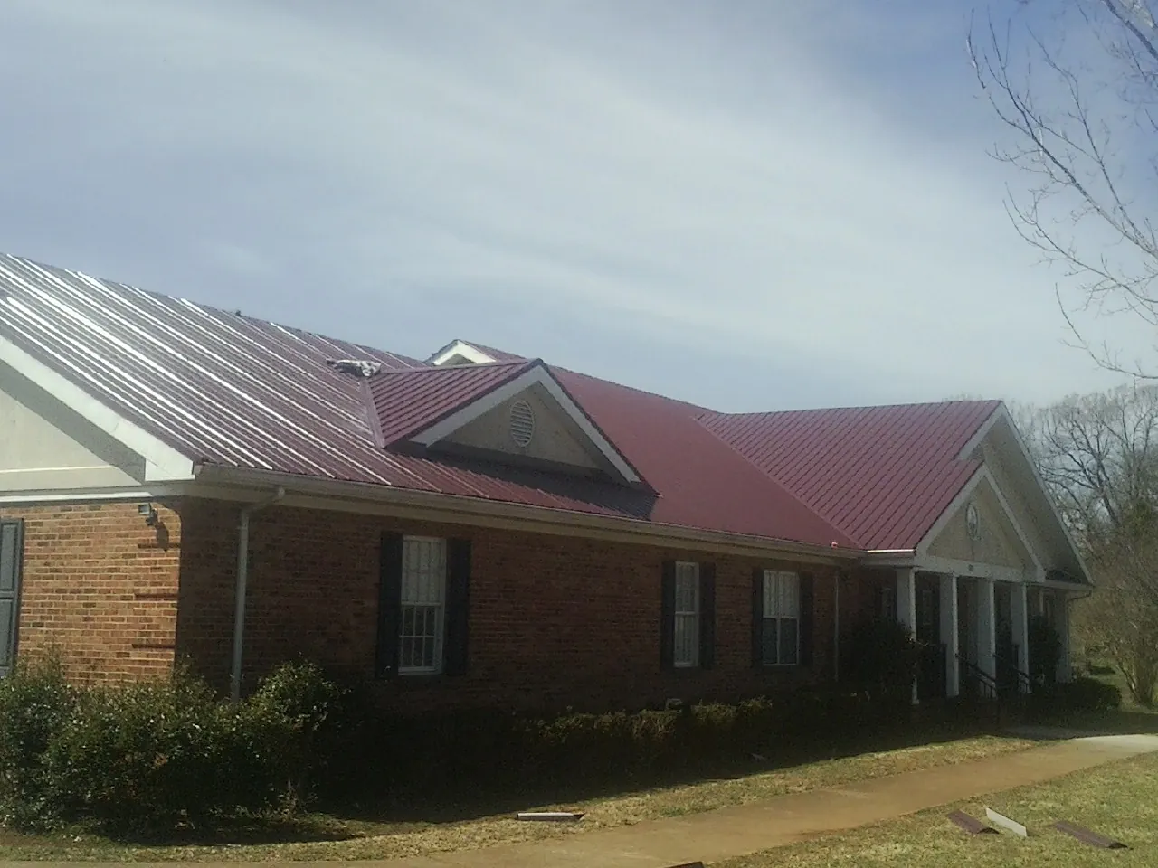 Red metal roof with gabled entries on a long brick building, from a Hail Damage Roof Repair job in Del Valle