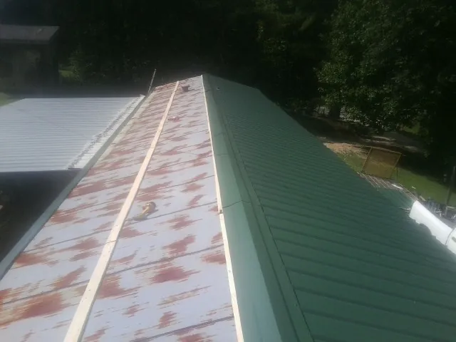 Old rusted panels beside newly installed green metal roofing — Wind Damage Roof Repair by Roofing Brothers in Del Valle