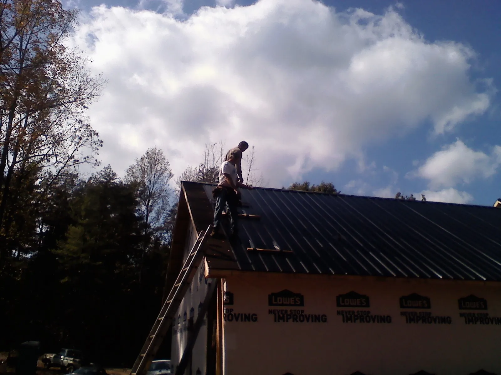 Roofer fastening dark metal panels high against a cloudy sky, from a Roof Inspection job in Del Valle