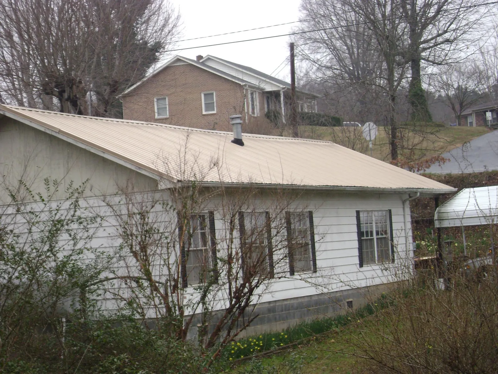 Tan metal roof on a white sided house set into a hillside — Commercial Roofing by Roofing Brothers in Del Valle